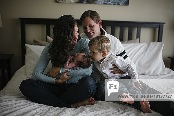 Familie mit neugeborenem Jungen zu Hause im Bett sitzend