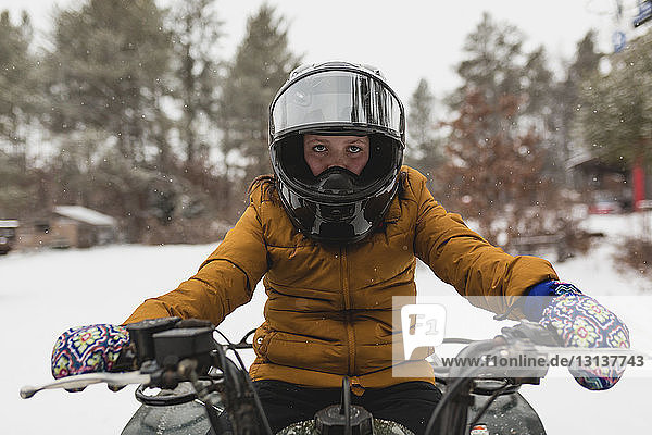 Portrait of girl snowmobiling on snow covered field in forest
