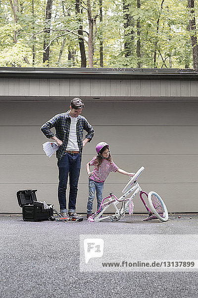 Mädchen zeigt dem Vater auf dem Bürgersteig ein kaputtes Fahrrad