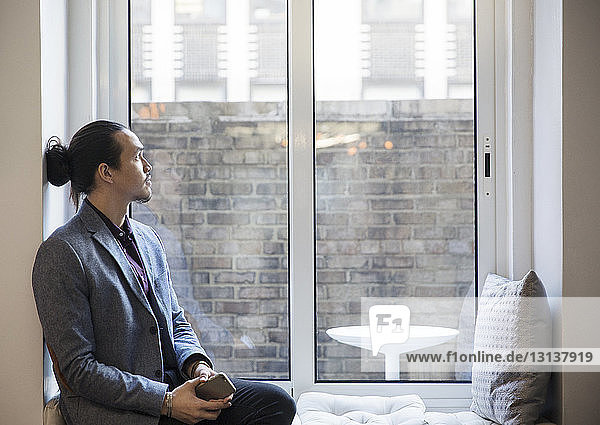 Thoughtful man looking through window while sitting in office