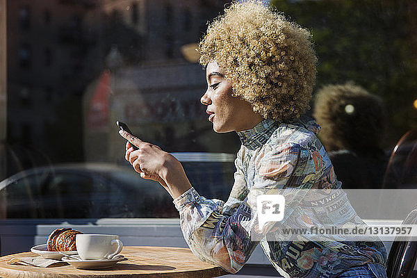 Seitenansicht einer Frau  die Textnachrichten verschickt  während sie am Tisch im Straßencafé sitzt