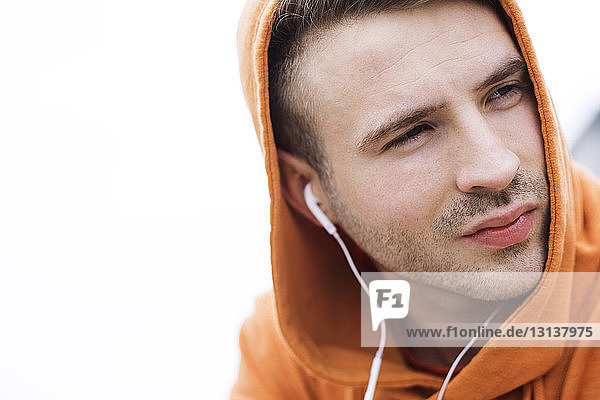 Close-up of thoughtful male athlete listening music against clear sky