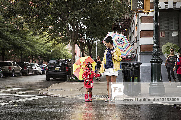 Mother and daughter looking at each other while holding umbrellas on street