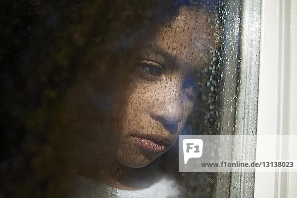 Trauriges Mädchen schaut durch nasses Fensterglas weg
