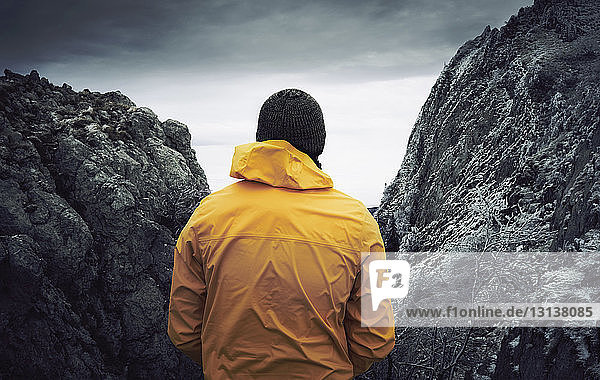 Rückansicht eines Mannes  der an Felsformationen vor bewölktem Himmel im Winter steht