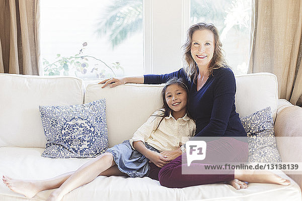 Portrait of smiling mother and daughter sitting on sofa at home
