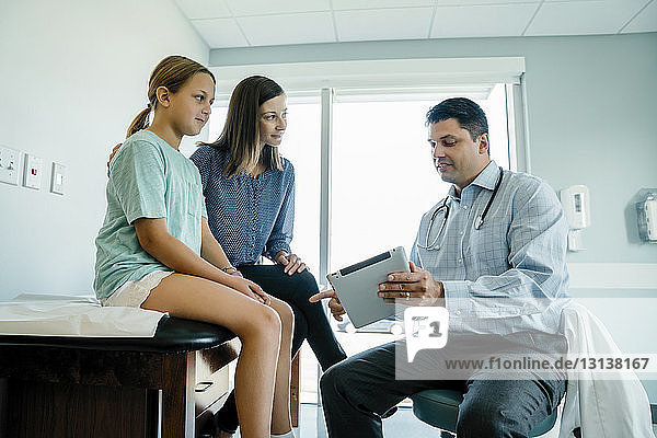 Kinderarzt diskutiert mit Mutter und Tochter über Tablet-Computer im medizinischen Untersuchungsraum
