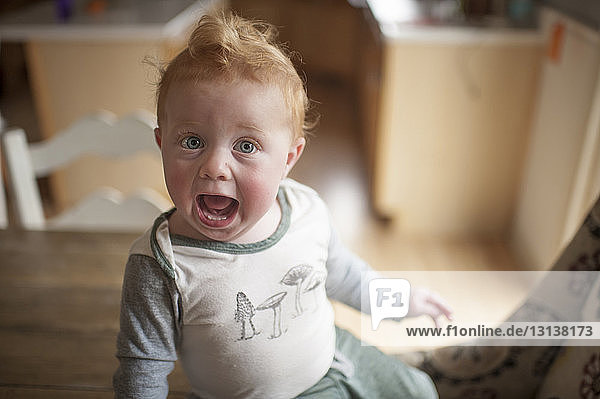 Hochwinkelporträt eines kleinen Jungen mit offenem Mund  der zu Hause auf einem Tisch sitzt