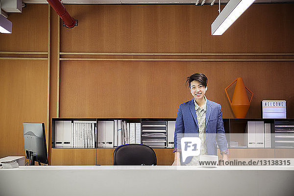 Porträt einer selbstbewusst lächelnden Geschäftsfrau  die im Büro am Schreibtisch steht