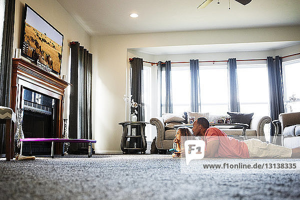 Vater und Tochter sehen fern  während sie zu Hause auf dem Teppich liegen