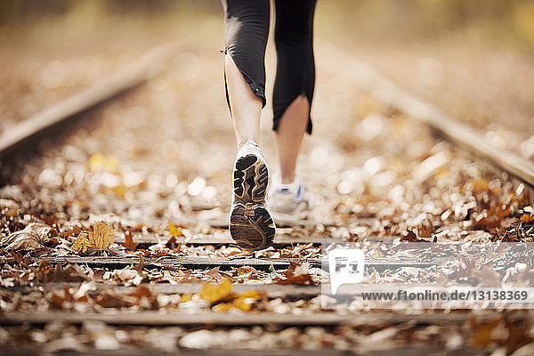 Low section of woman jogging on railroad track during autumn