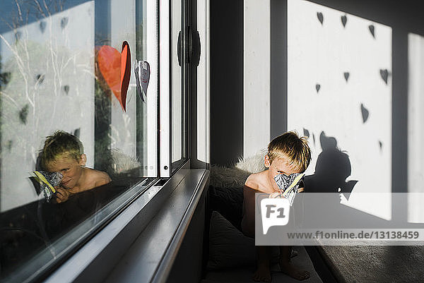 Junge ohne Hemd beim Dekorieren  während er zu Hause am Fenster sitzt