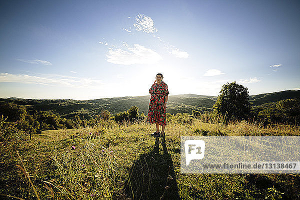 Portrait of woman standing on grassy field against sky