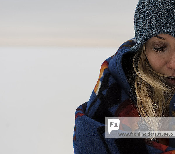 Beschnittenes Bild einer in eine Decke gehüllten Frau  die auf einer schneebedeckten Landschaft vor dem Himmel steht