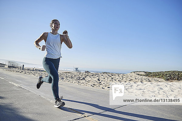 Full length of woman jogging on road by beach against clear sky