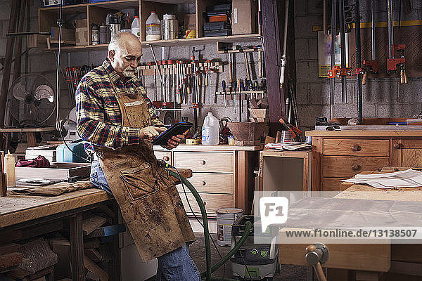 Leitender Handwerker benutzt digitales Tablett  während er in der Werkstatt steht