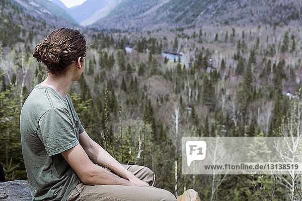 Thoughtful hiker sitting on mountain against trees