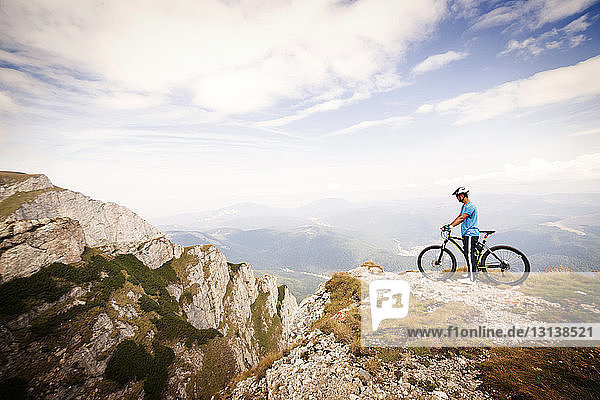 Side view of mountain biker with bicycle against cloudy sky