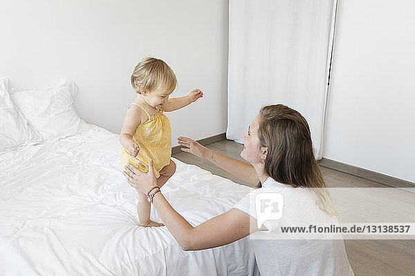 Hochwinkelansicht einer glücklichen Mutter  die ihre Tochter zu Hause im Bett laufen sieht