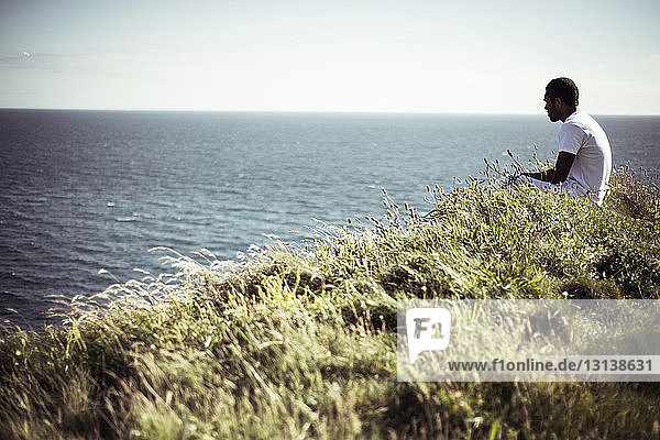 Seitenansicht eines Mannes  der auf einem Feld am See sitzt