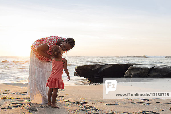 Mutter küsst Tochter  während sie am Strand gegen den Himmel steht