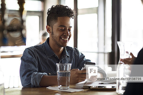 Lächelnder junger Mann am Telefon an der Theke eines Cafés