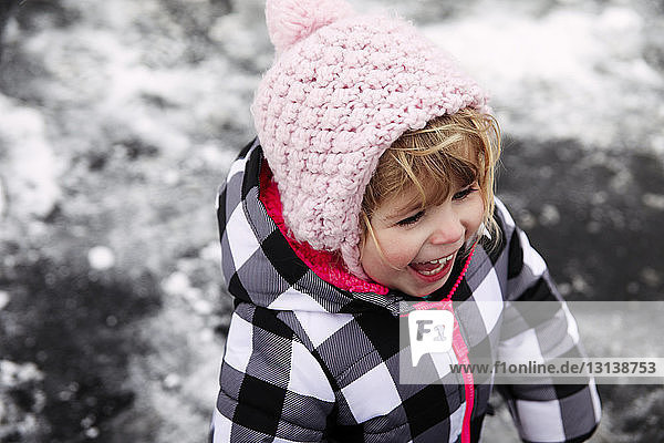 Hochwinkelaufnahme eines fröhlichen Mädchens  das im Winter auf der Straße steht