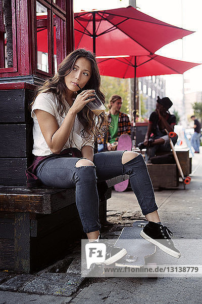 Thoughtful woman drinking smoothie juice while sitting on retaining wall