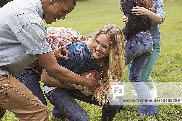 Male friends snatching football ball from woman on grassy field