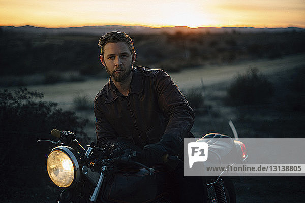 Portrait of man riding motorcycle on field during sunset