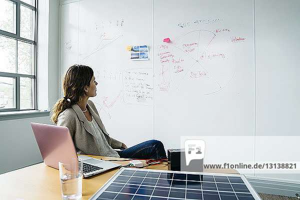 Businesswoman looking at diagram on whiteboard while working over solar panel in office