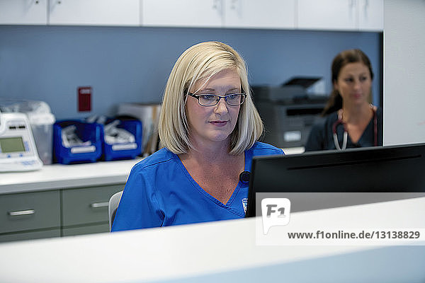 Female doctor using desktop computer with colleague in background