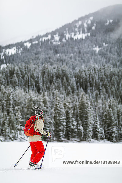 Frau mit Rucksack beim Wandern in schneebedeckter Landschaft