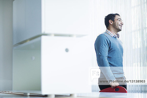 Smiling businessman standing by table in office