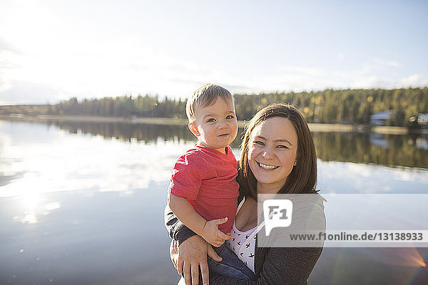 Portrait of mother and son against lake during sunny day