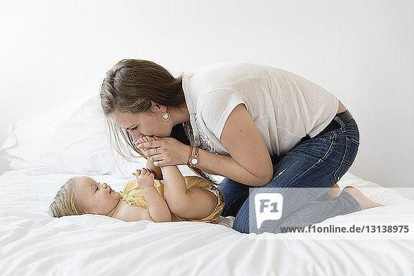 Side view of mother playing with daughter on bed at home
