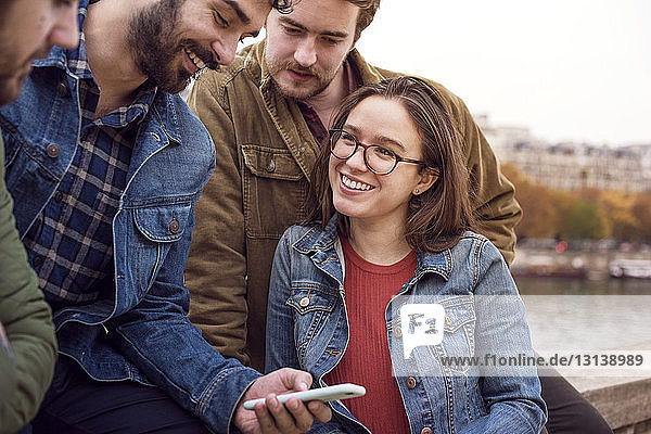 Glücklicher Mann benutzt Smartphone mit Freunden  während er auf Stützmauer sitzt
