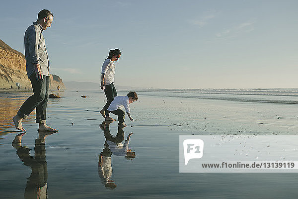 Eltern sehen Sohn beim Pflücken von Kieselsteinen vom Ufer am Strand gegen den Himmel