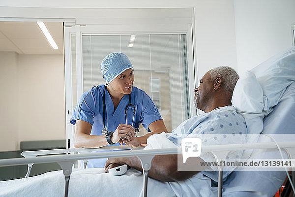 Surgeon talking with senior patient lying on bed in hospital ward