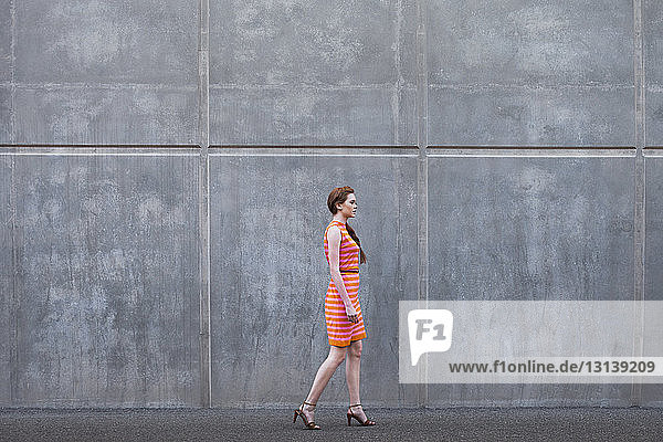 Side view of young woman walking on sidewalk against wall