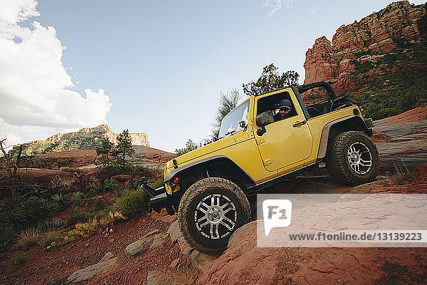 Yellow off-road vehicle moving down on rocks at mountain against sky
