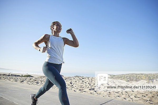 Woman jogging on road by beach against clear sky