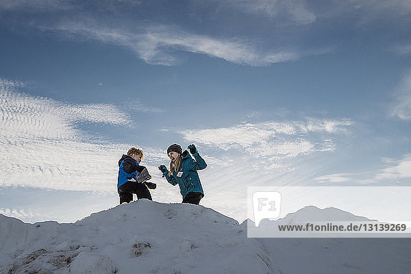 Low angle view of siblings on snow against sky