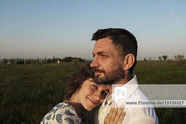 Portrait of PRegnant woman embracing man on field against clear sky