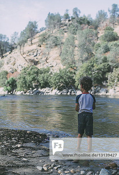 Rear view of boy fishing while standing in lake against mountains