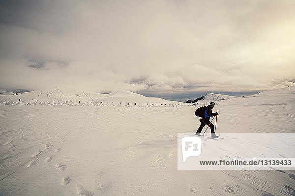 Side view of skier walking on snow against cloudy sky