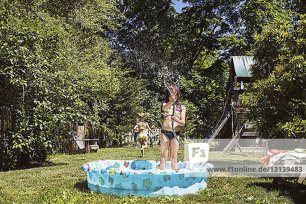 Girl playing with water while standing in wading pool at yard