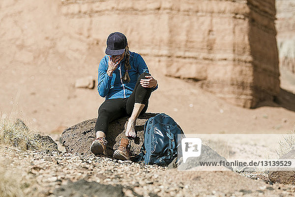 Müde Wanderin mit Rucksack entspannt sich am sonnigen Tag auf einem Felsen in der Wüste