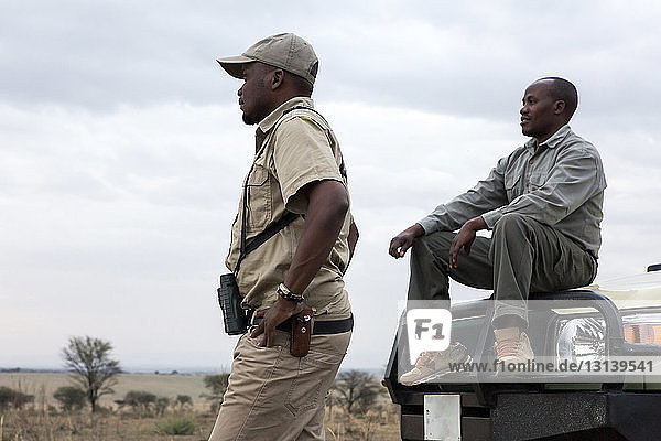 Männliche Freunde mit Geländewagen gegen bewölkten Himmel im Serengeti-Nationalpark