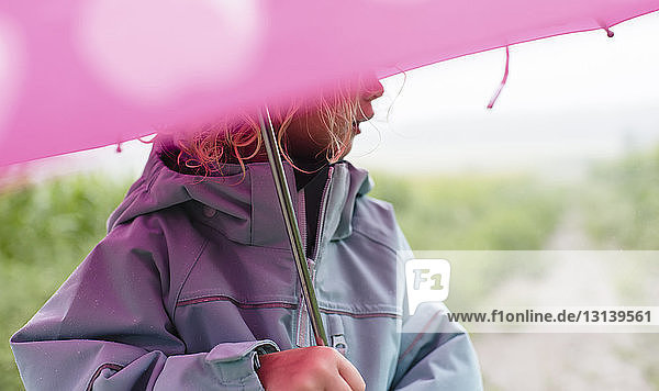 Midsection of girl carrying umbrella while standing outdoors during rainy season